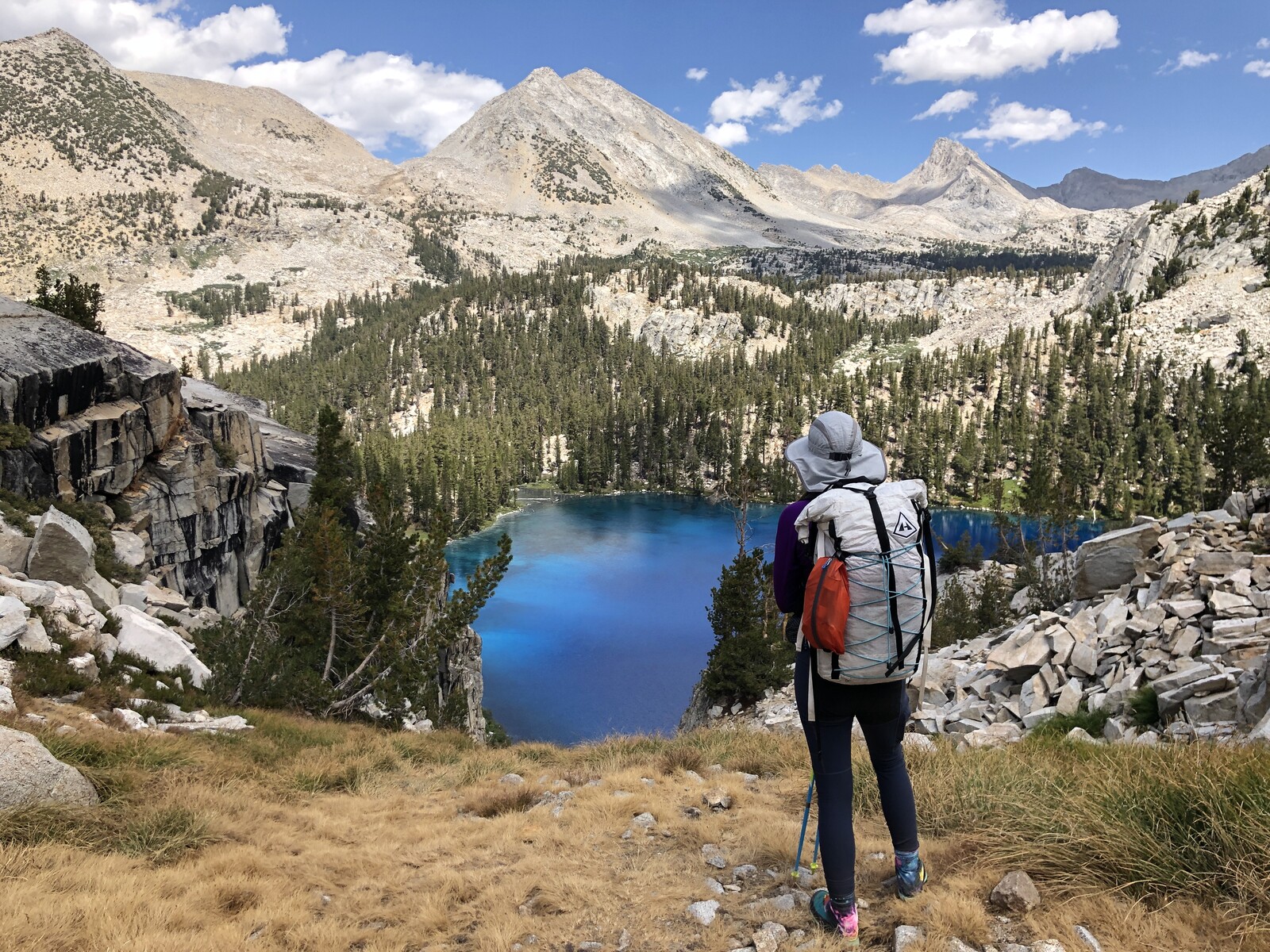Hiker with backpack overlooking turquoise alpine lake and peaks