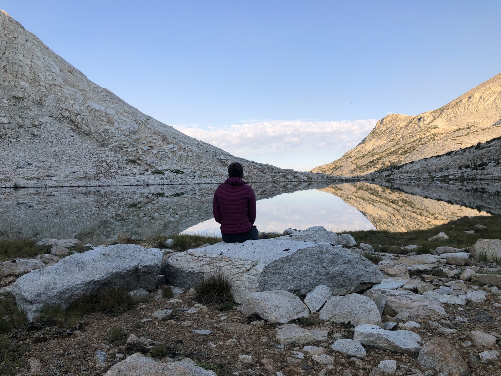 Lone hiker meditating beside mirror-like alpine lake