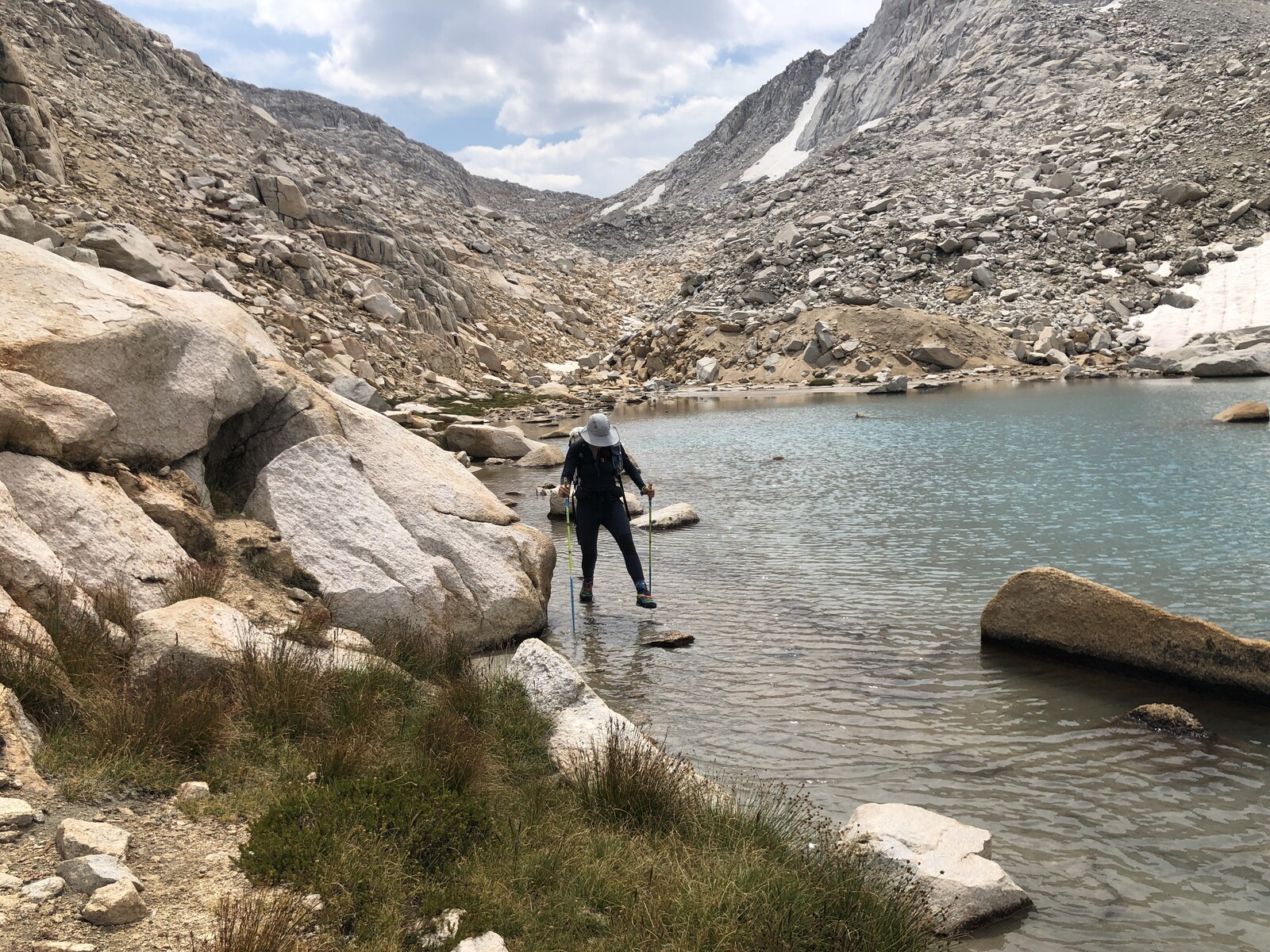 Hiker wading in turquoise alpine lake surrounded by peaks