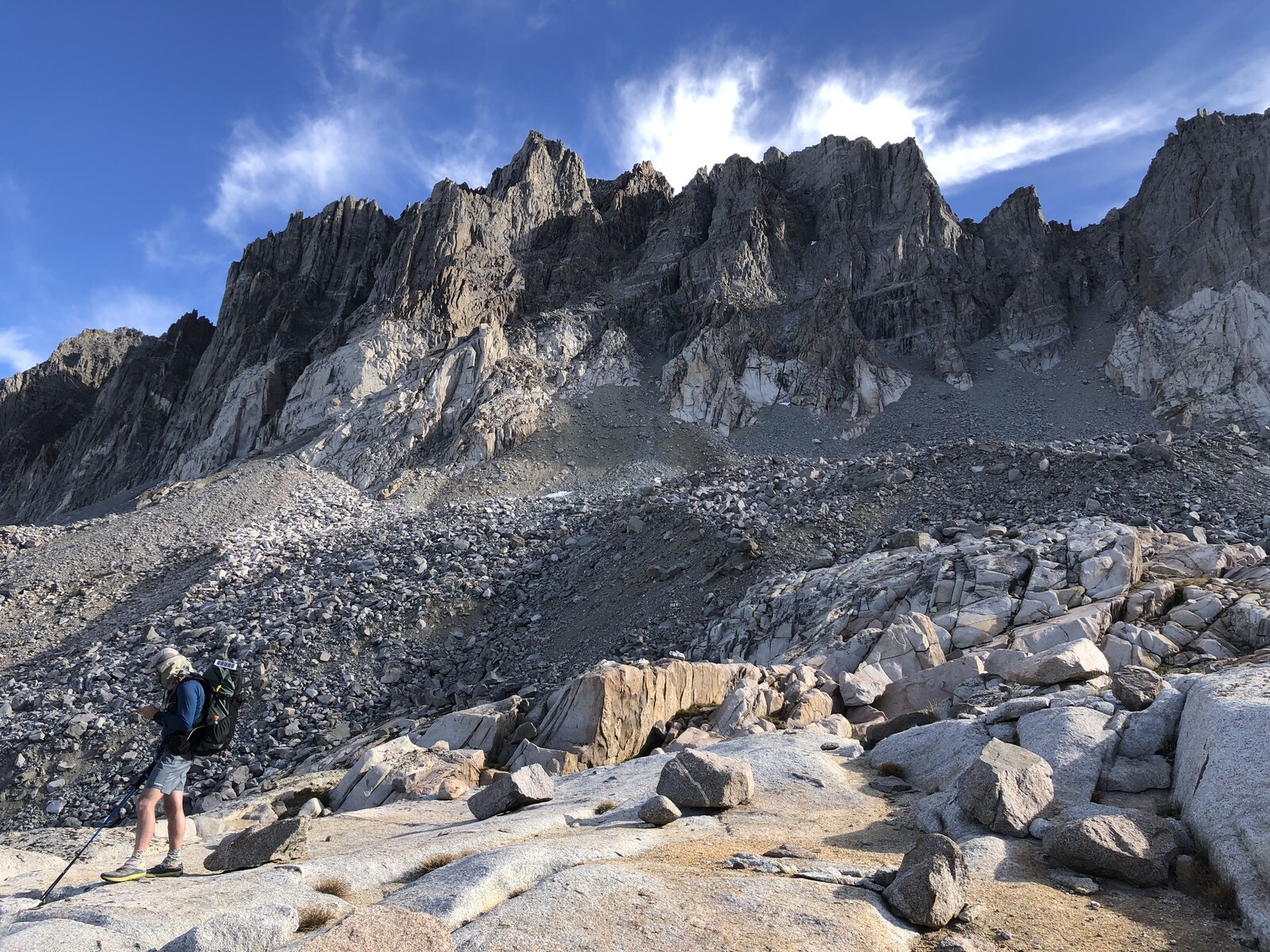 Hiker ascending talus slope toward jagged mountain face