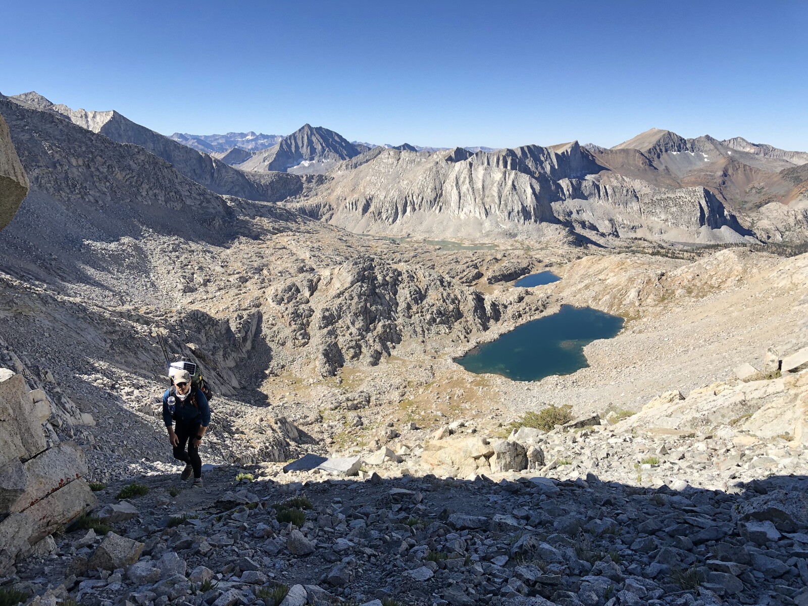 Expansive view of hiker in alpine cirque with turquoise lake
